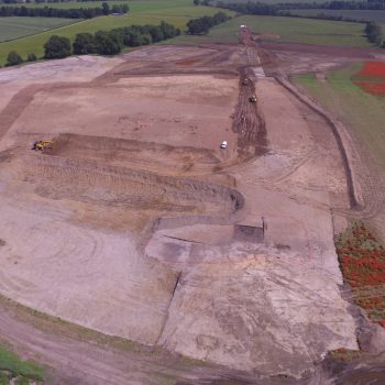 A view of the site with one of the wetland areas surrounded by orange fencing in the foreground and our team excavating to the left of the white van. Can you spot the two enclosures in the top left of the photo?