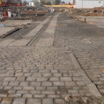 External, sett stone surface courtyard that dissected the two main buildings of the Poplar Grove Bleach and Dye Works. To the west (left) were several machine rooms as well as the boiler beds, furnaces and chimney stack. To the east (right) was the main shop floor largely associated with the dying processes © Copyright ARS Ltd 2022